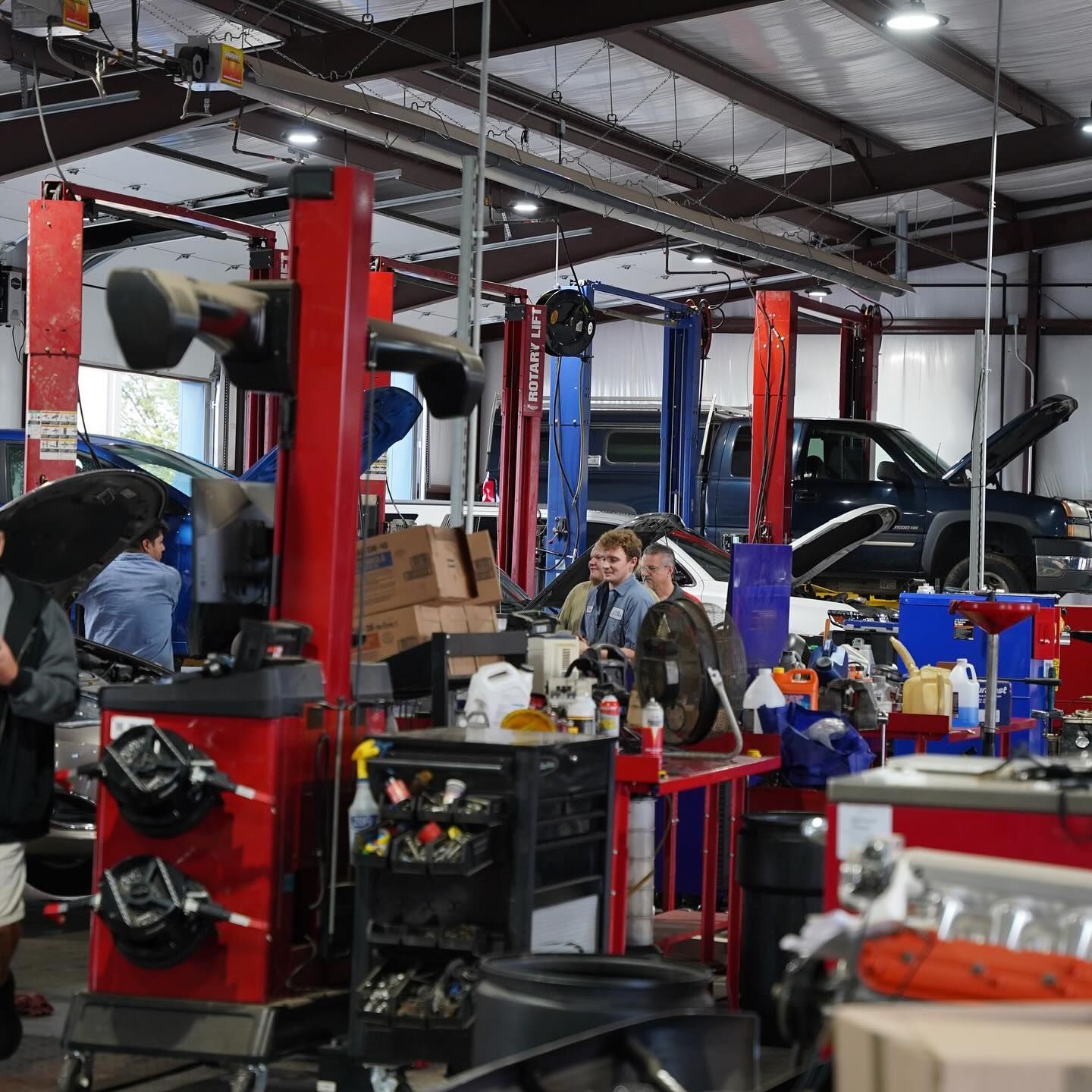 An auto repair shop interior with people working on vehicles, tools, and lifts.