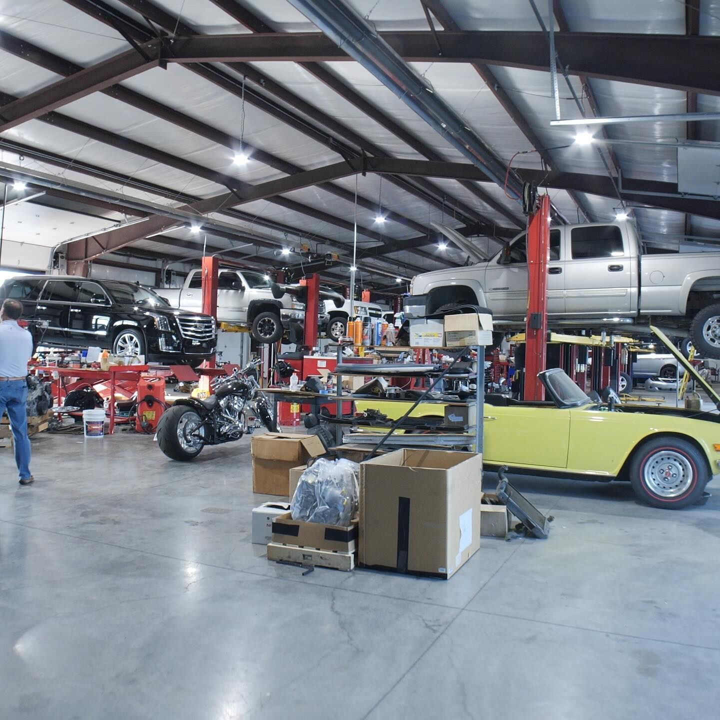 Inside auto repair shop with vehicles on lifts, tools, and a person standing near a motorcycle.