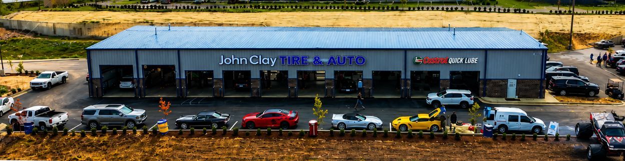 John Clay Automotive with parked cars along the front and a grassy hillside behind it