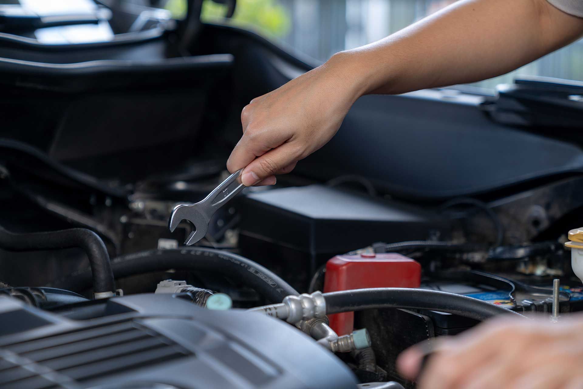 A close-up view of a hand holding a wrench over an open car engine bay.