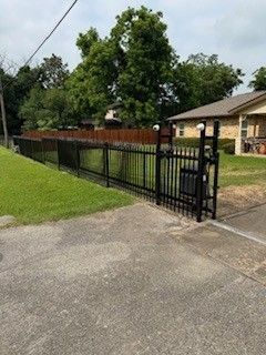 A black fence surrounds a driveway in front of a house.