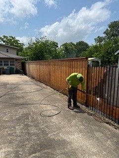 A man is cleaning a wooden fence with a pressure washer.