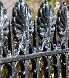 A close up of a black wrought iron fence with leaves on it