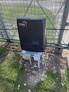 A black box is sitting in the grass next to a fence.