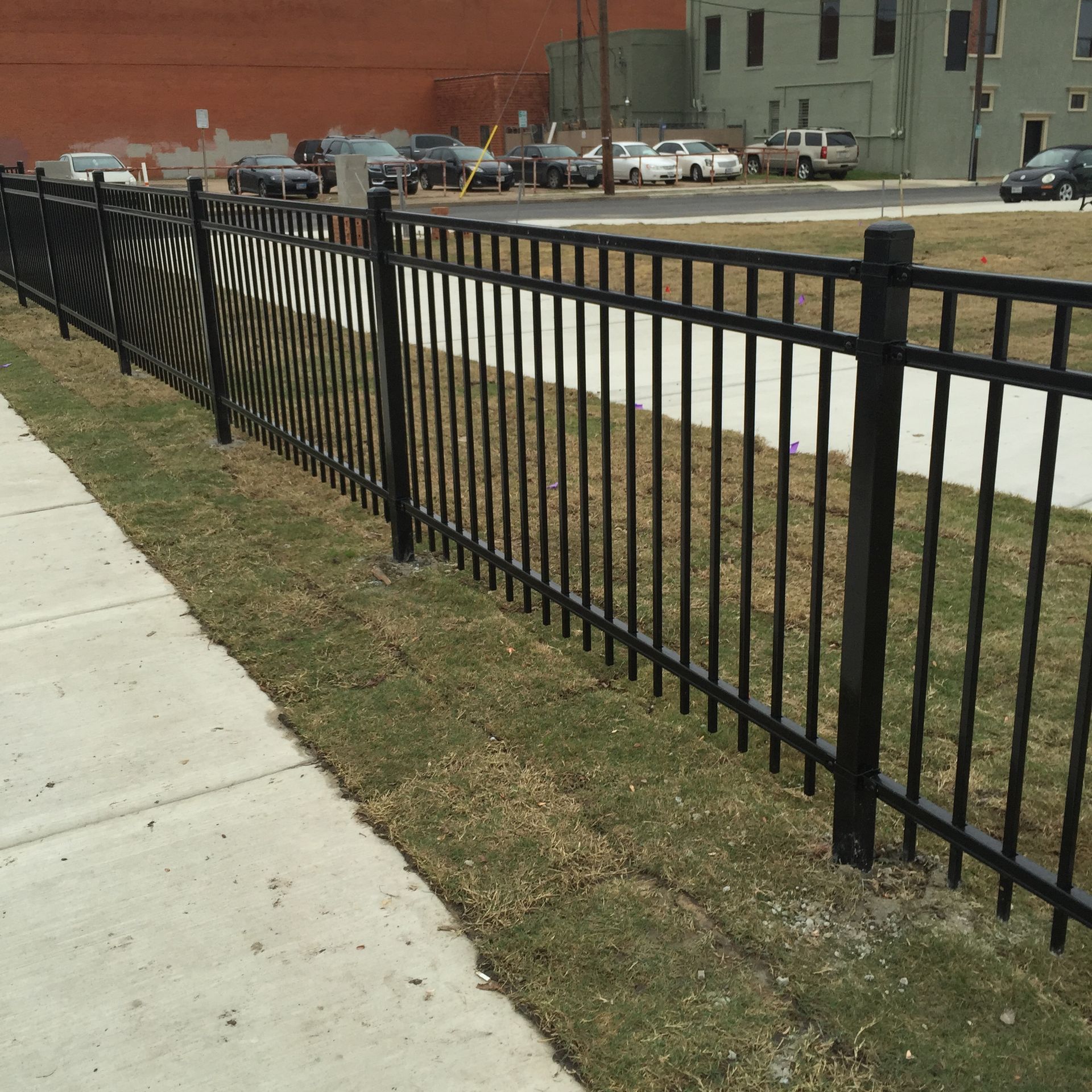 A black fence along a sidewalk with cars parked behind it