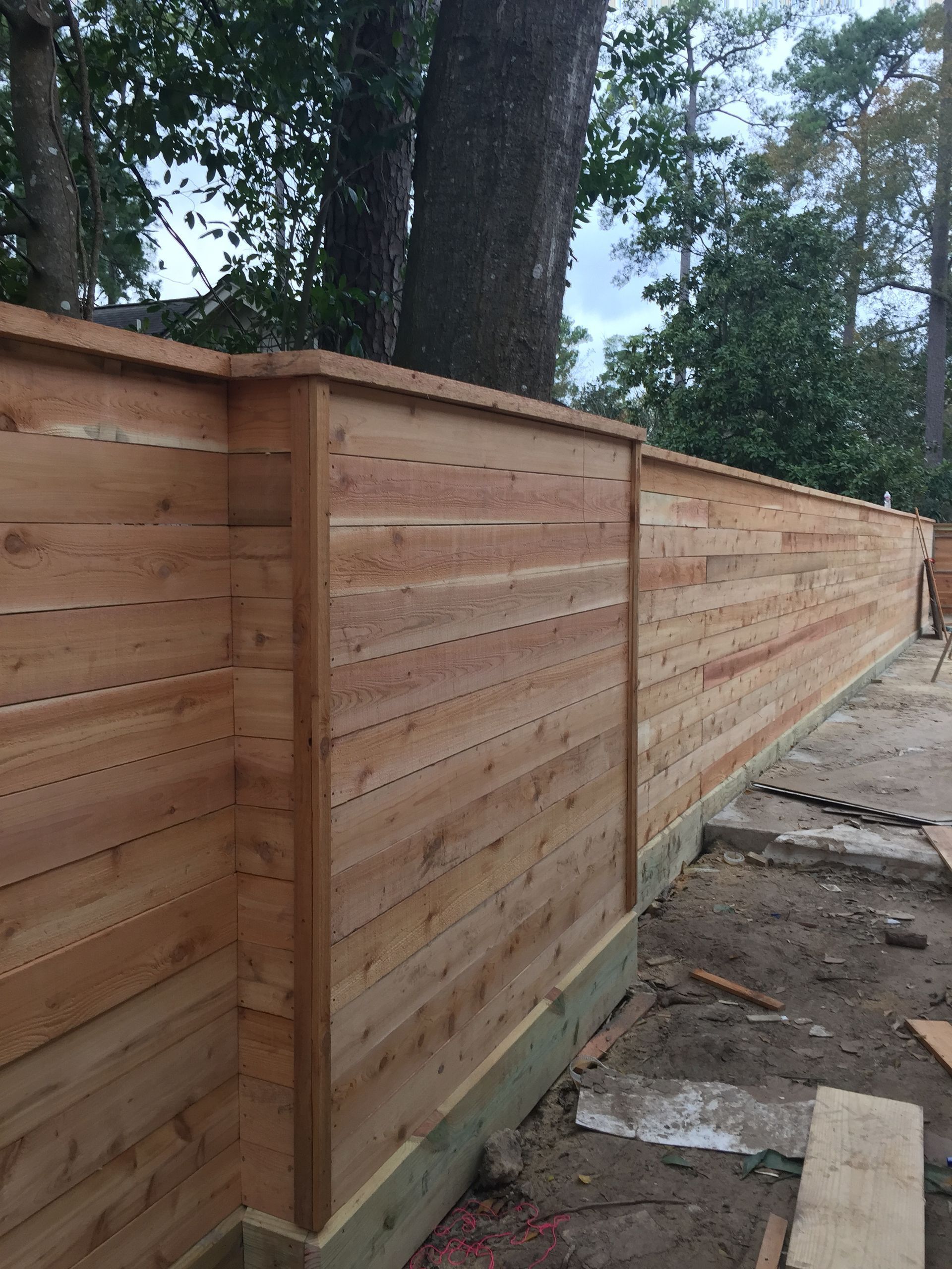 A wooden fence is being built in a backyard with trees in the background.