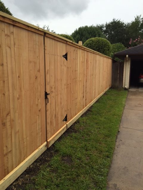 A wooden fence is sitting next to a driveway next to a garage.