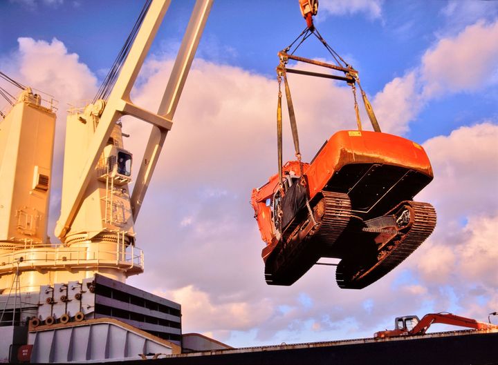 Large crane lifting an orange excavator against a cloudy sky