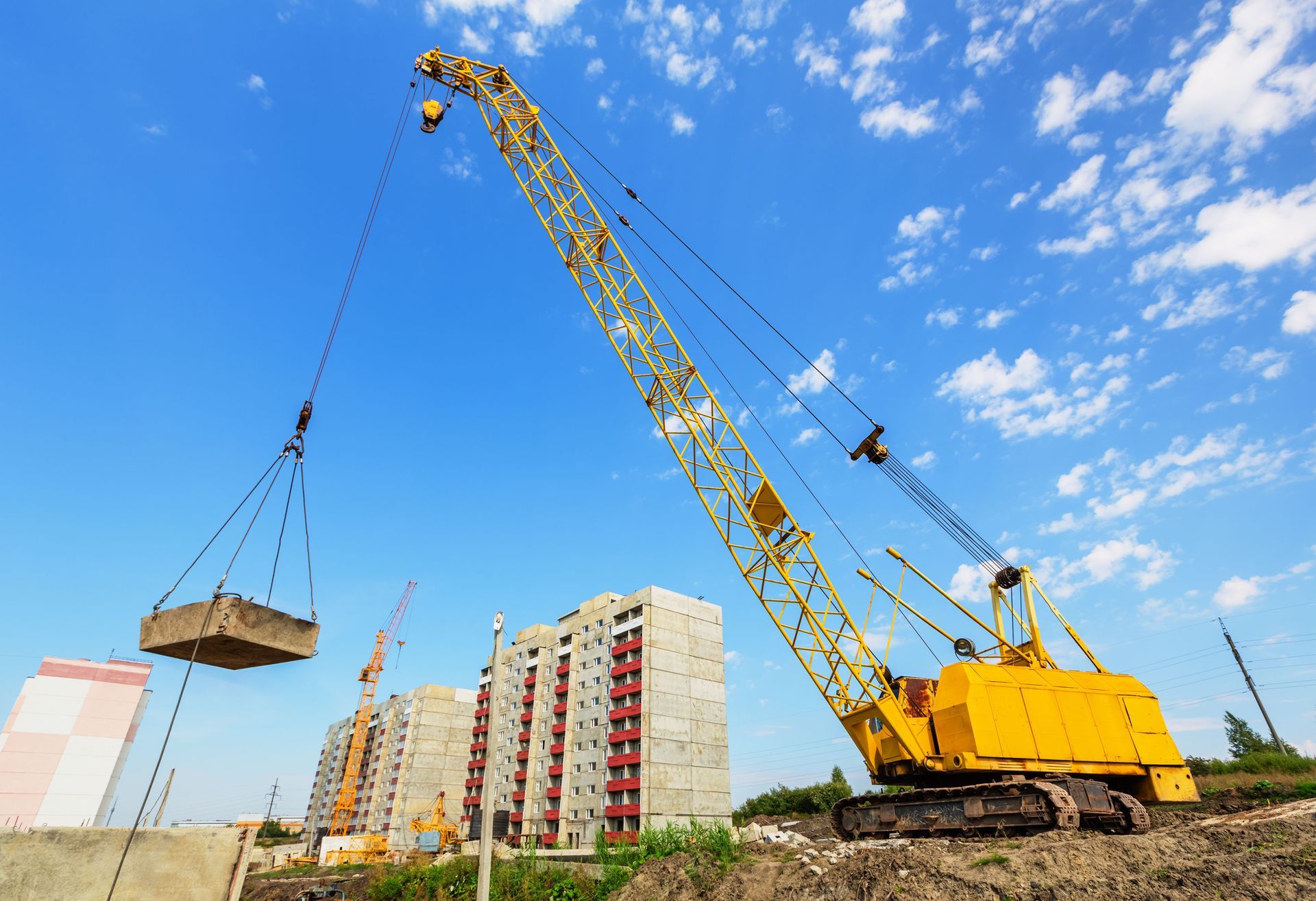 Crawler crane lifting large concrete slab near buildings