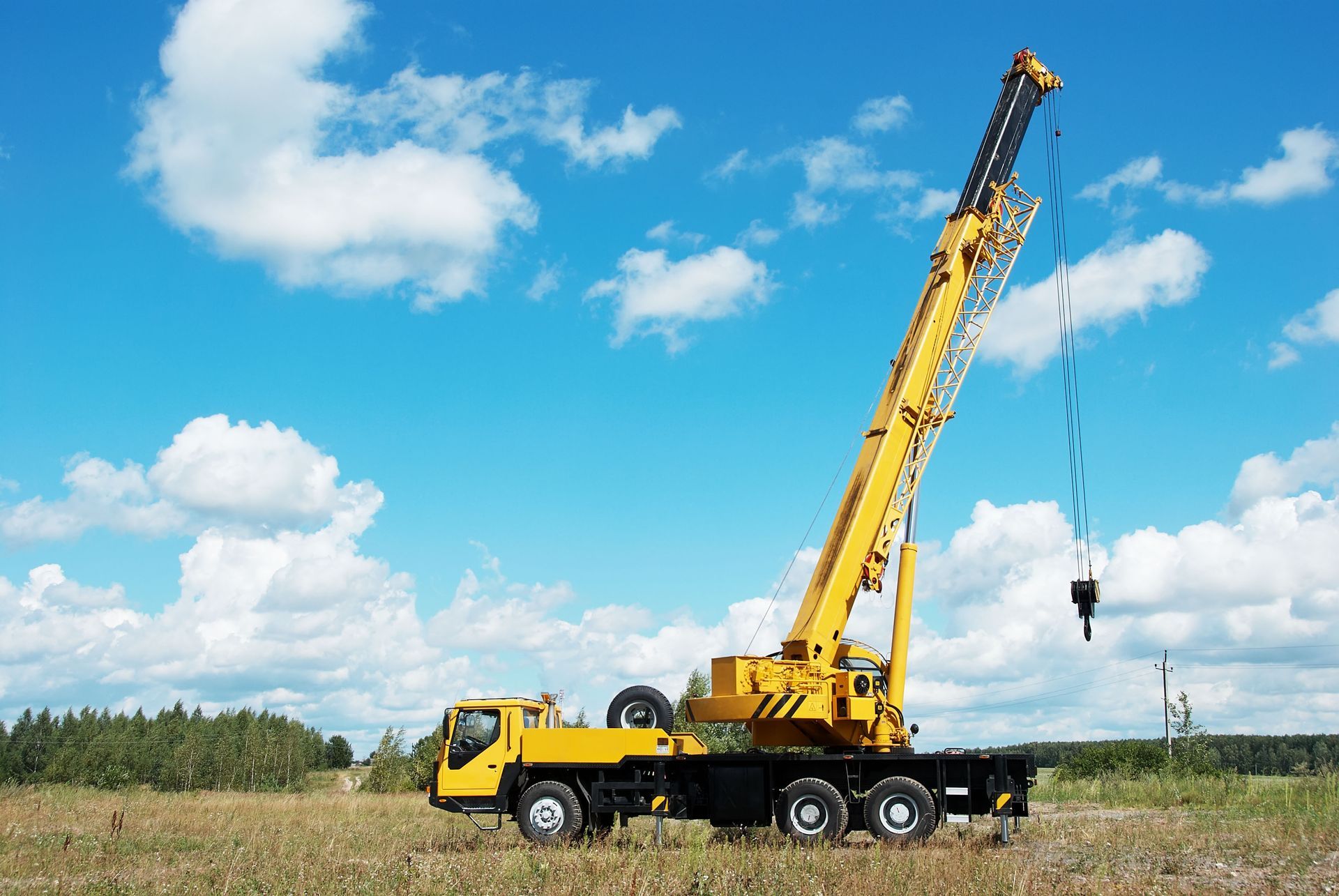 Yellow mobile crane with long boom in open field