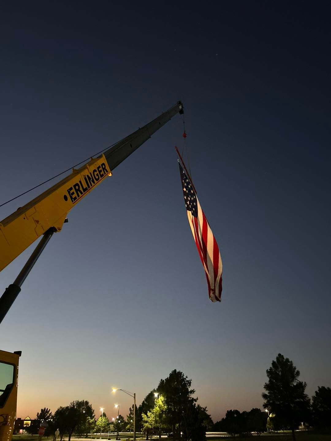 A yellow Erlanger crane is lifting an American flag