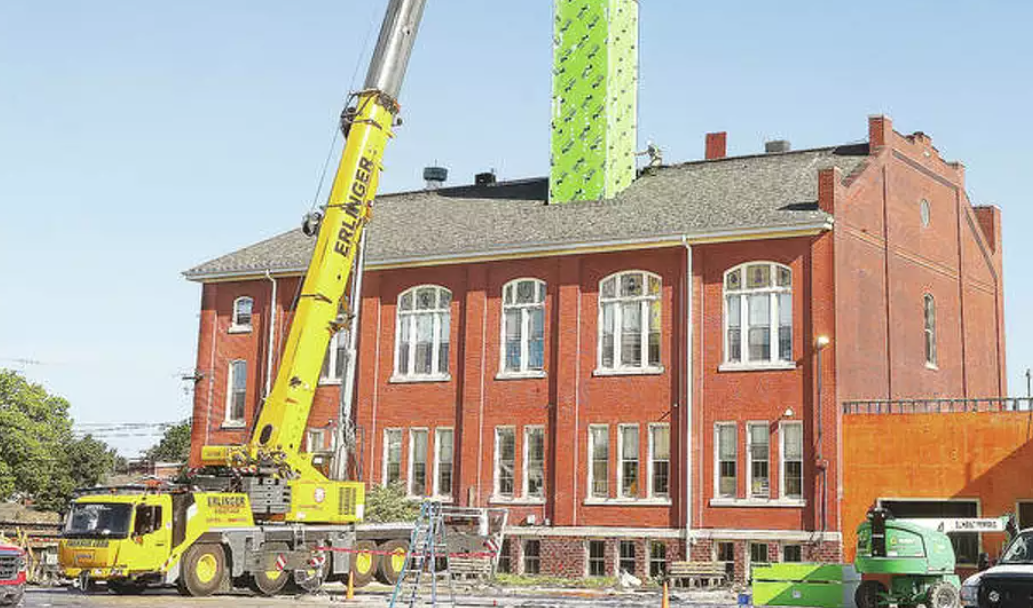 A large yellow crane is sitting in front of a large brick building