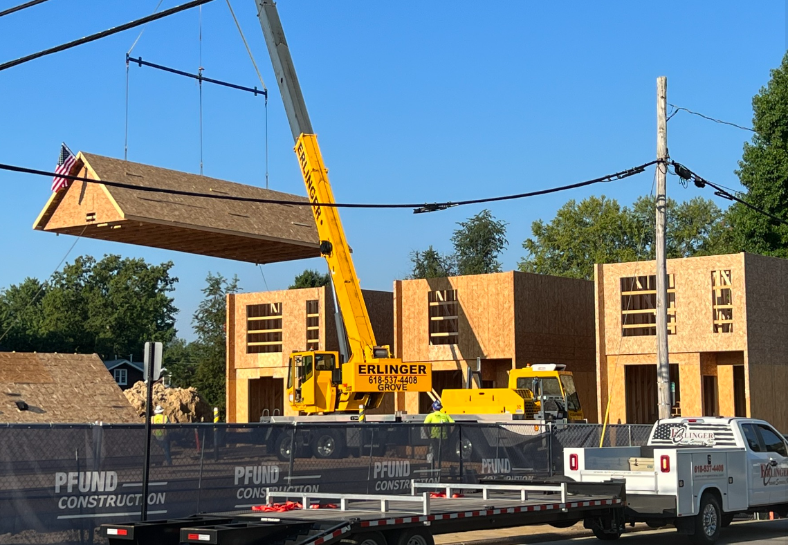 A crane is lifting a piece of wood on top of a building under construction