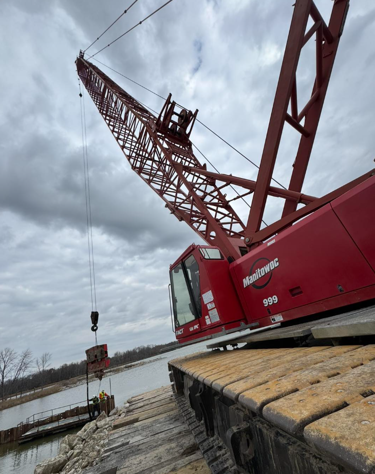 A large red crane is sitting on a wooden platform near a body of water.