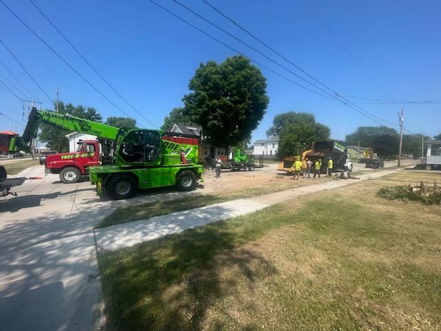 Construction scene with several green and yellow vehicles and workers on a sunny day in a residential area.