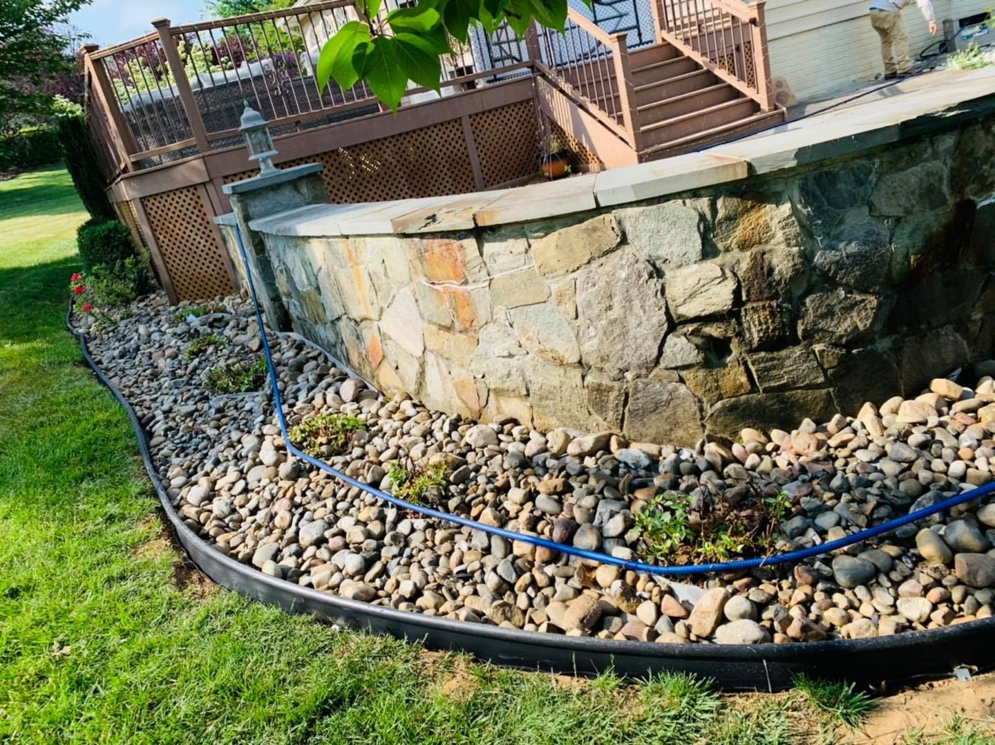 Curved stone retaining wall with blue hose and rocks in a landscaped yard
