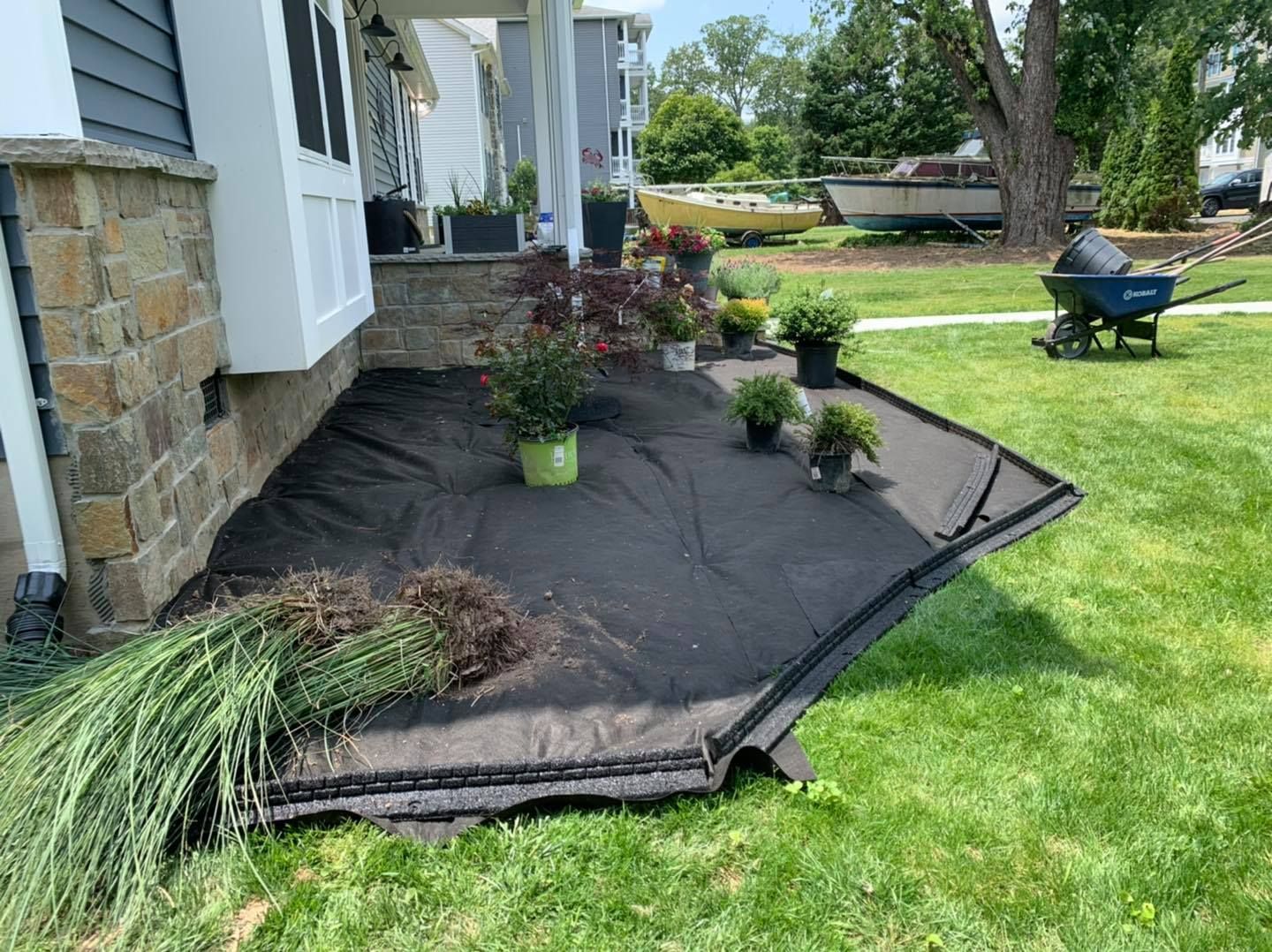 Black landscape fabric border with small potted shrubs along a house and green lawn