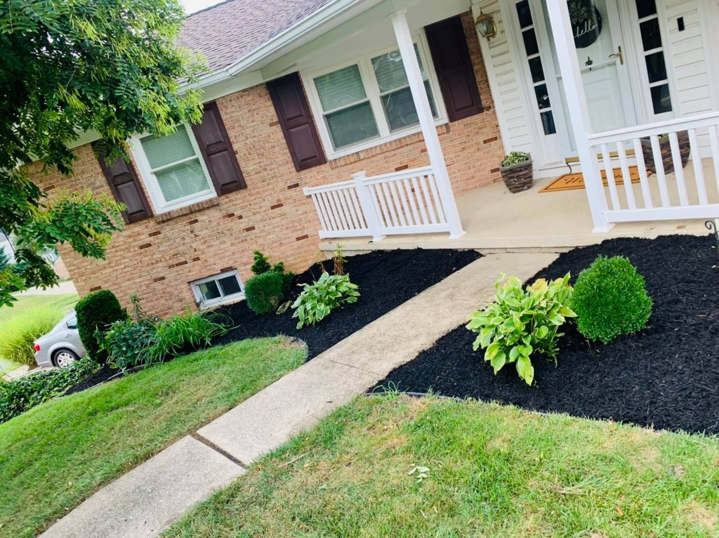Brick house with white porch, brown shutters, and landscaped front yard with mulch and walkway