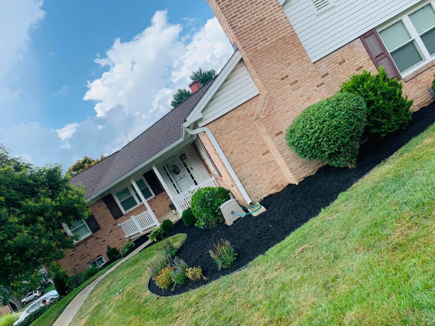 Brick suburban house with white trim, green lawn, and neatly landscaped front yard under a blue sky