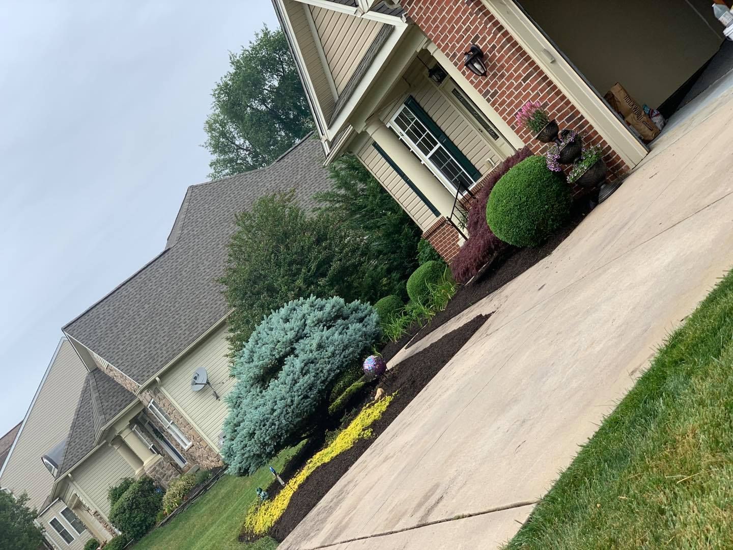 Suburban house with brick facade, driveway, and manicured shrubs beside a flower bed on a sloped lawn