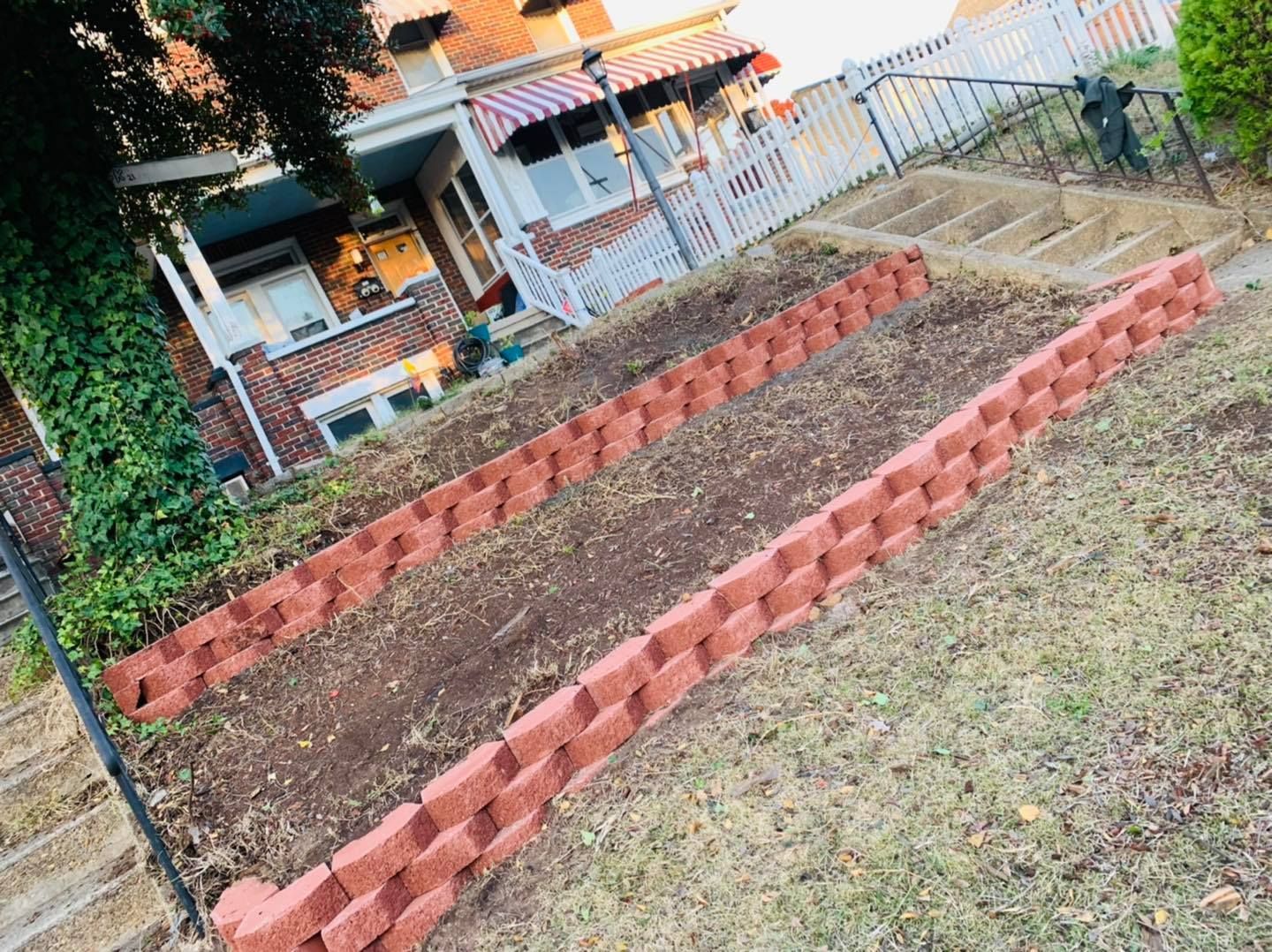 Raised red brick garden beds in a grassy yard beside a house and fence.
