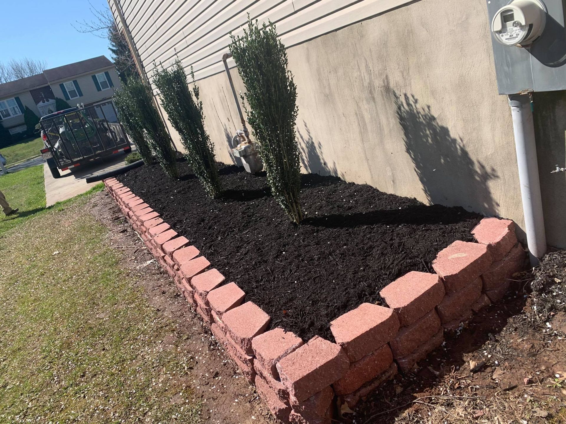 Raised brick-edged garden bed with dark mulch and small shrubs beside a house exterior