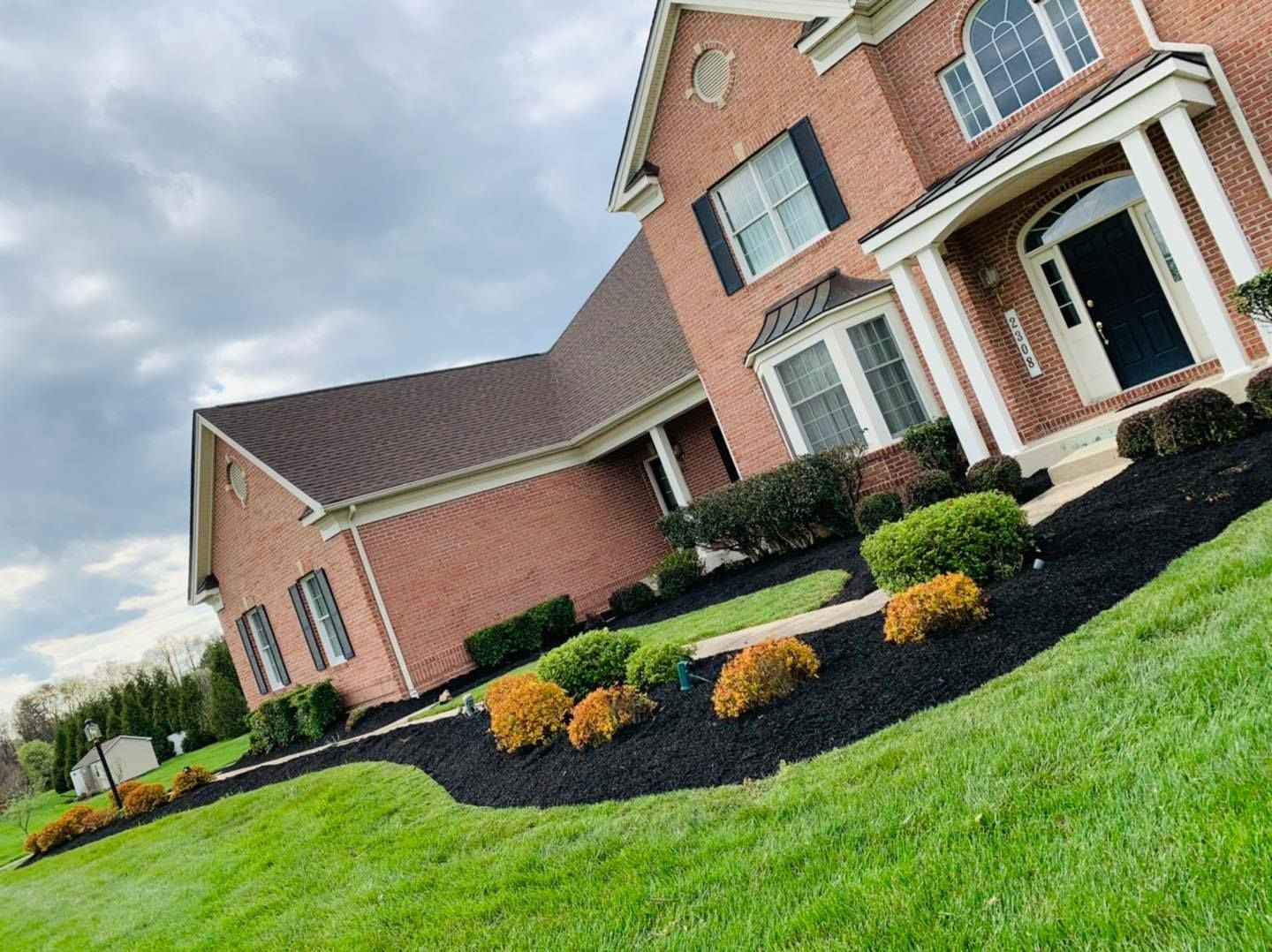 Brick suburban house with manicured lawn, dark mulch landscaping, and cloudy sky
