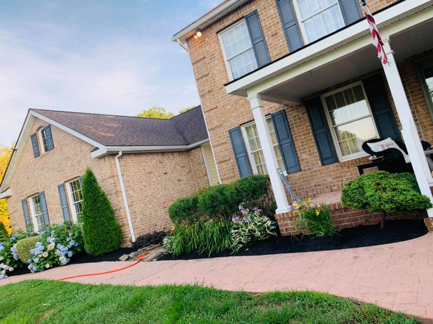 Suburban brick house with white columns, manicured shrubs, and a curved driveway under a cloudy sky