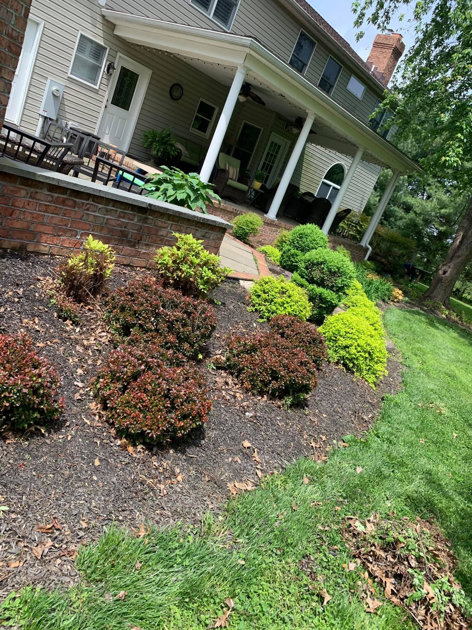 Front porch of a white house with arched columns and a landscaped flower bed of shrubs and mulch