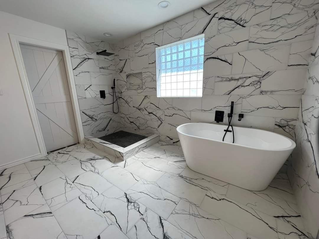 A bathroom with marble tiles , a tub , a shower and a window.