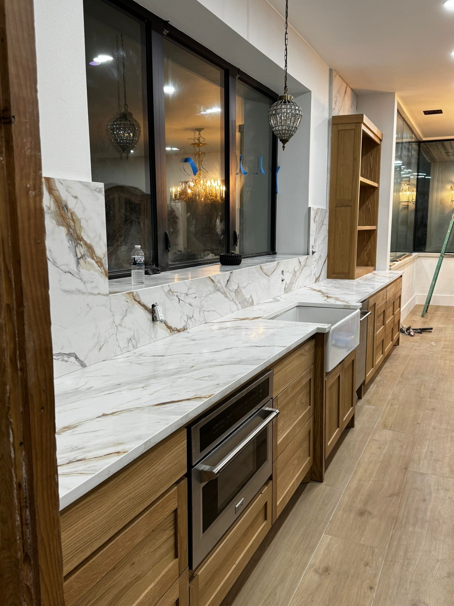 A kitchen with marble counter tops , wooden cabinets , stainless steel appliances and a large window.