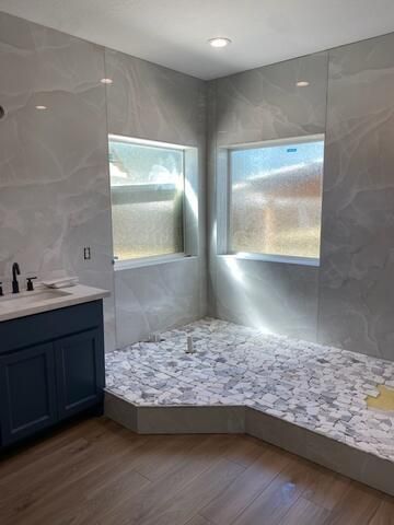 A bathroom with a sink , shower , and two windows.