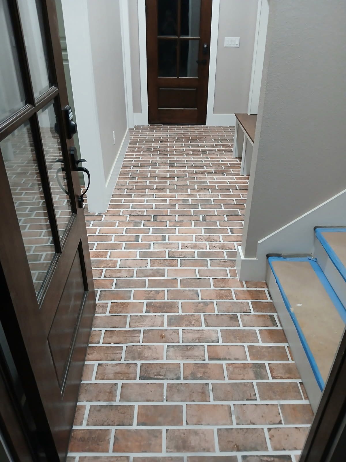 A hallway with a brick floor and stairs in a house.