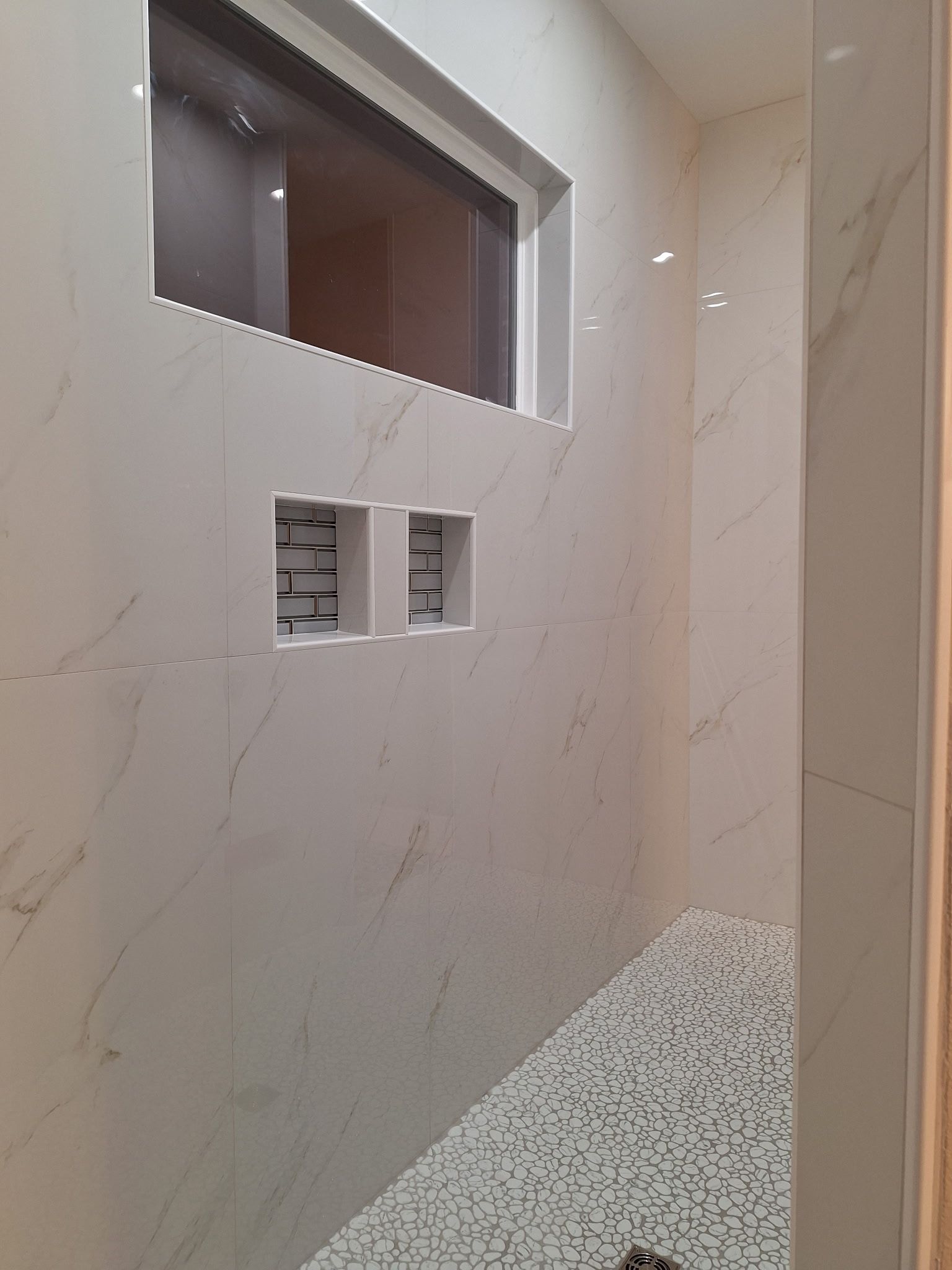 A bathroom with a walk in shower and a window.