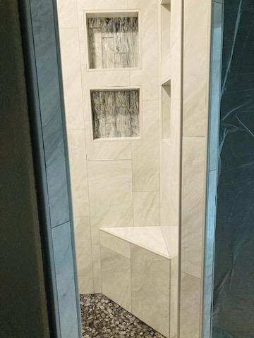 A bathroom with a walk in shower with a bench and shelves.