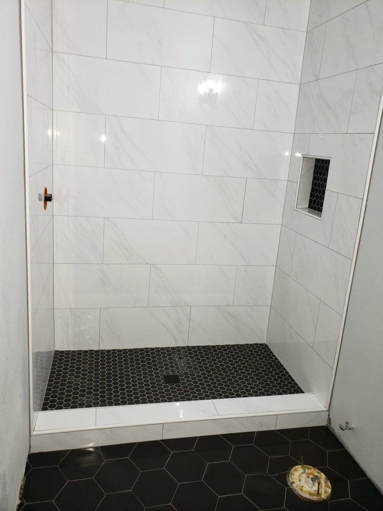A bathroom with white tiles and black tiles and a walk in shower.