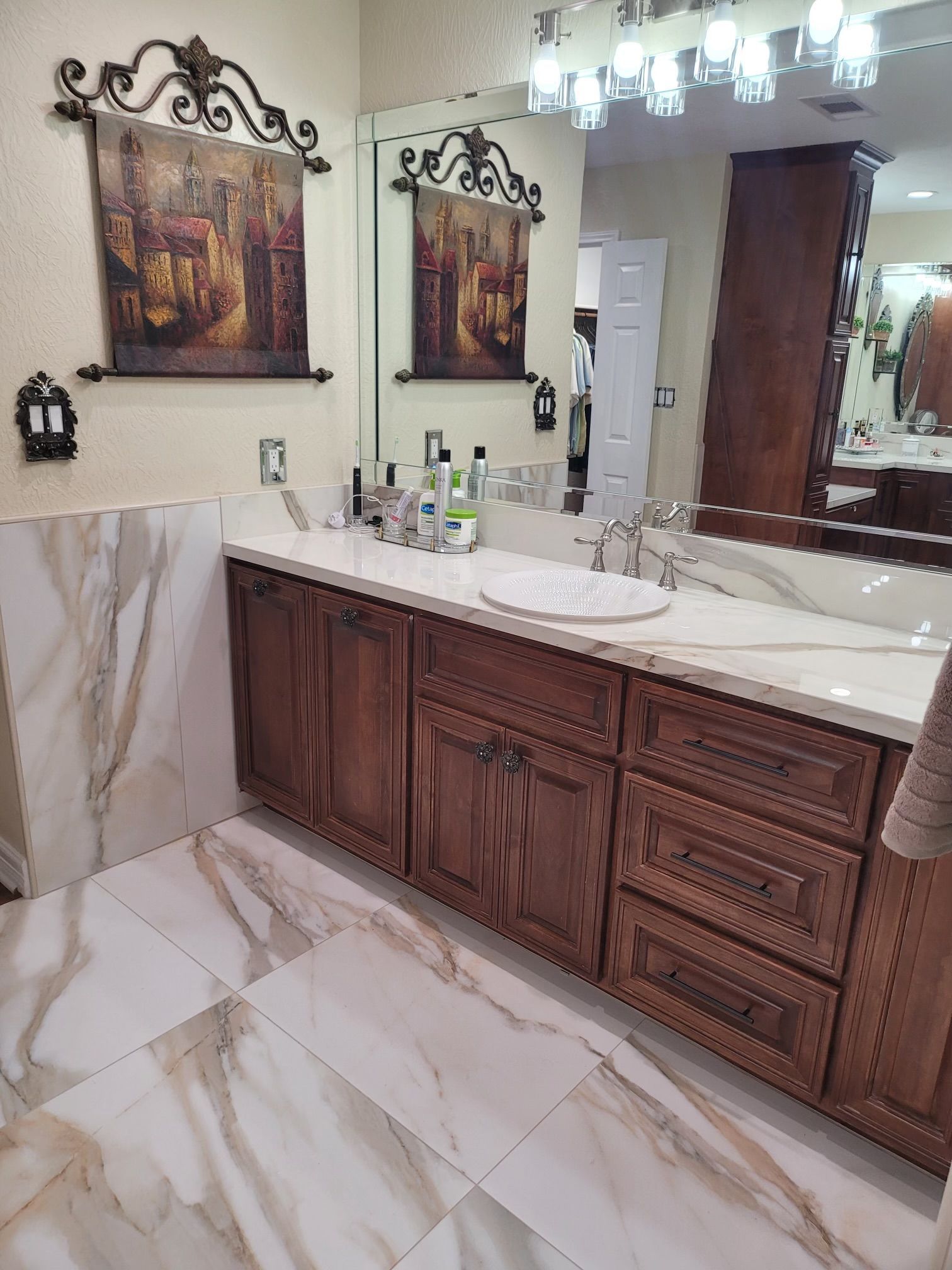 A bathroom with a sink , mirror , cabinets , and tile floor.