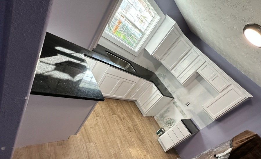 A kitchen with white cabinets and black granite counter tops.