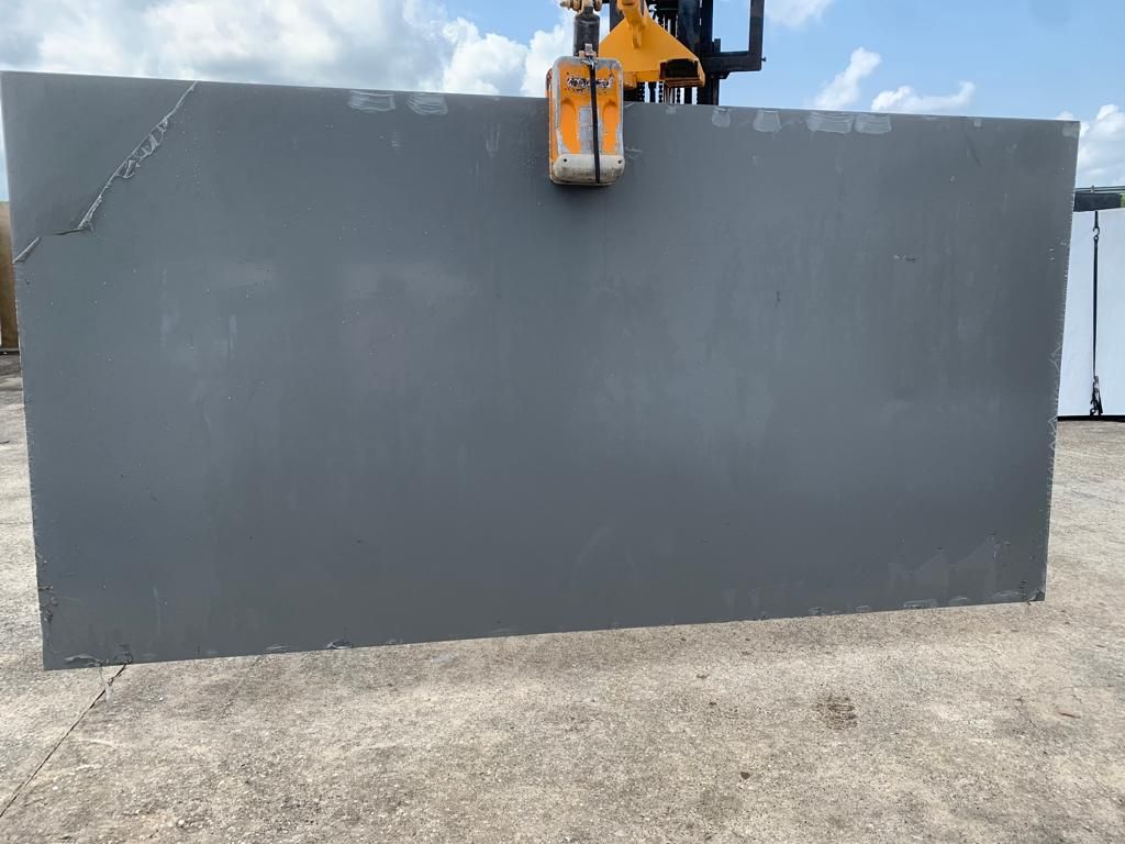 A large gray slab of granite is being lifted by a forklift.