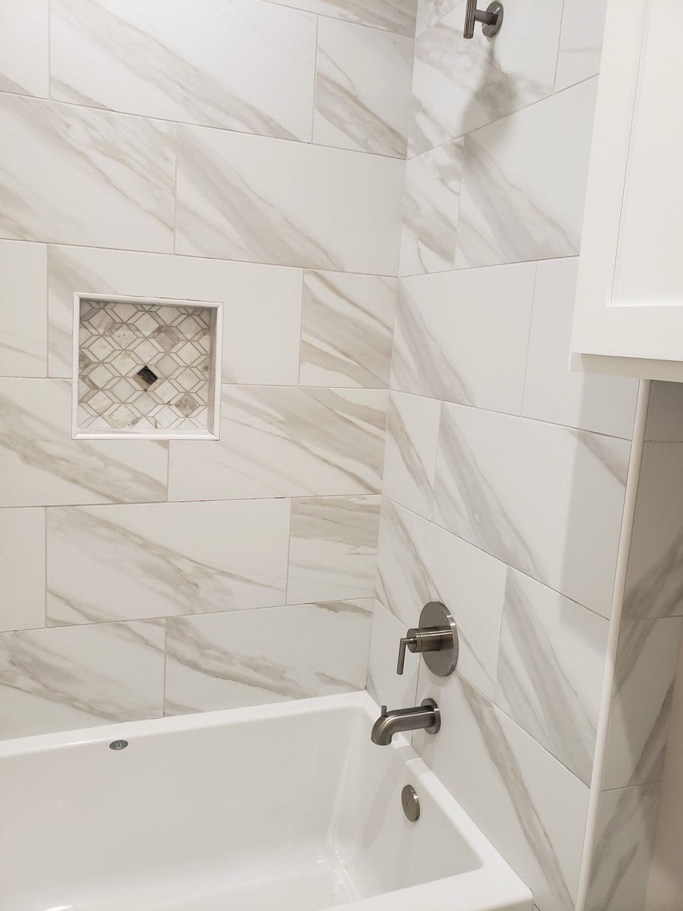 There is a bathtub in the bathroom with marble tiles on the wall.
