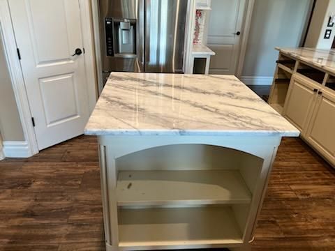 A kitchen with a marble counter top and a refrigerator.