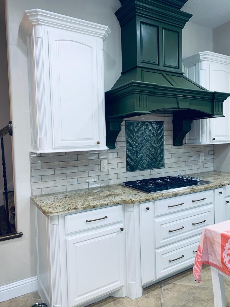 A kitchen with white cabinets , granite counter tops , and a green hood.