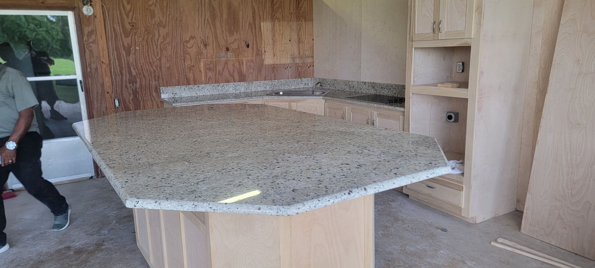 A man is standing next to a large granite counter top in a kitchen.