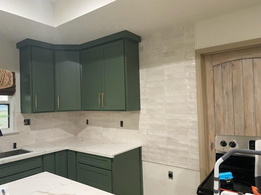 A kitchen with green cabinets and white counter tops.
