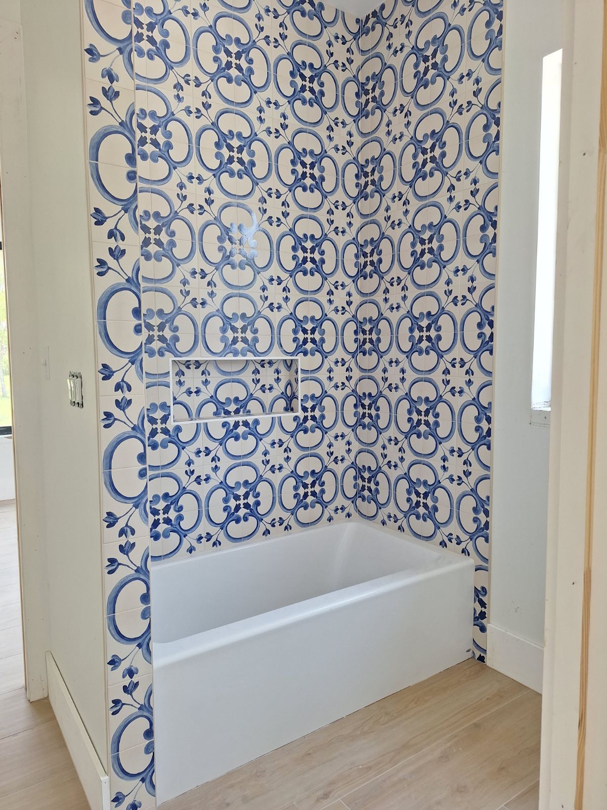 A bathroom with a bathtub and blue and white tiles on the wall.