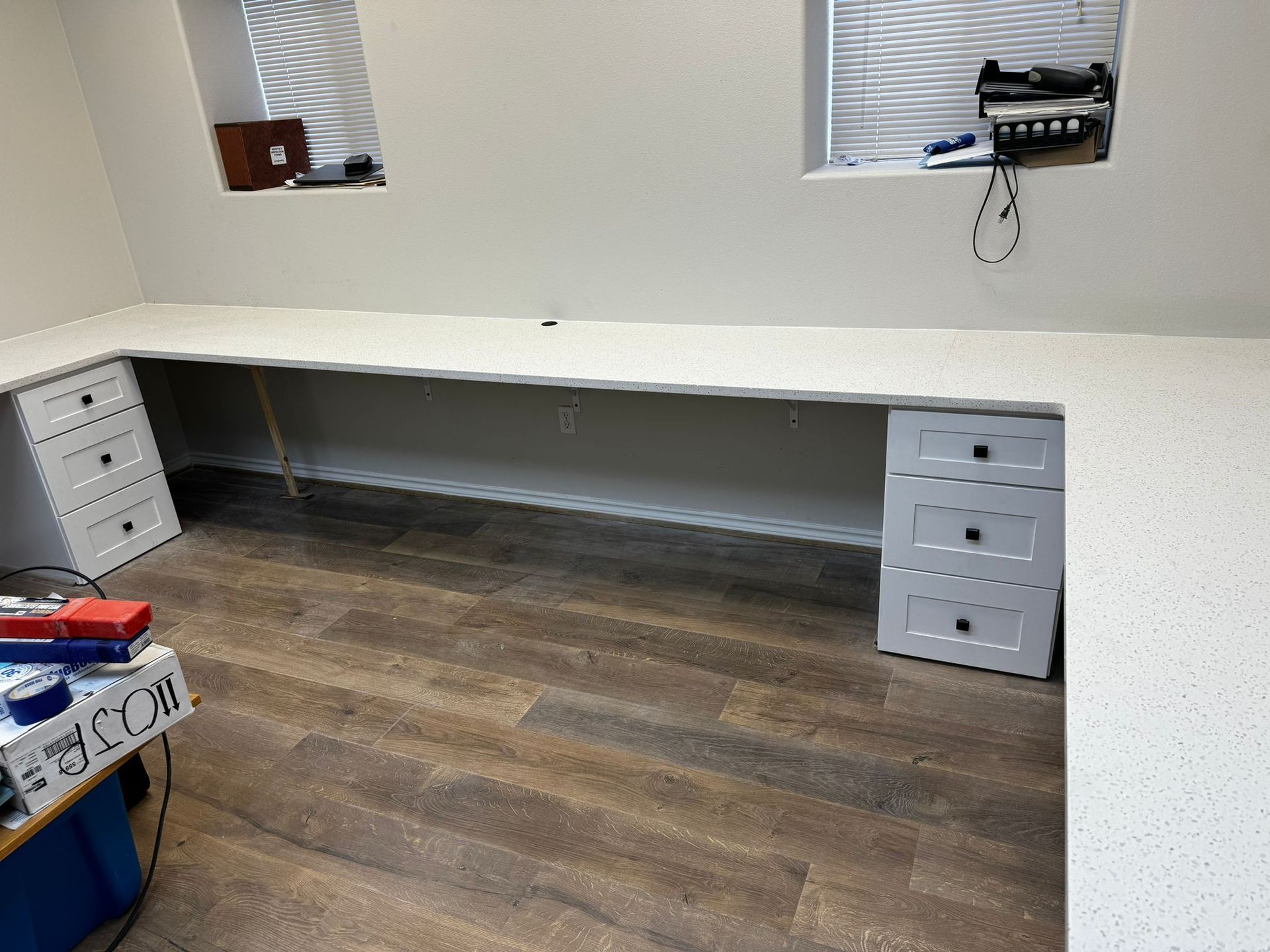 A room with a long desk and drawers and a window.