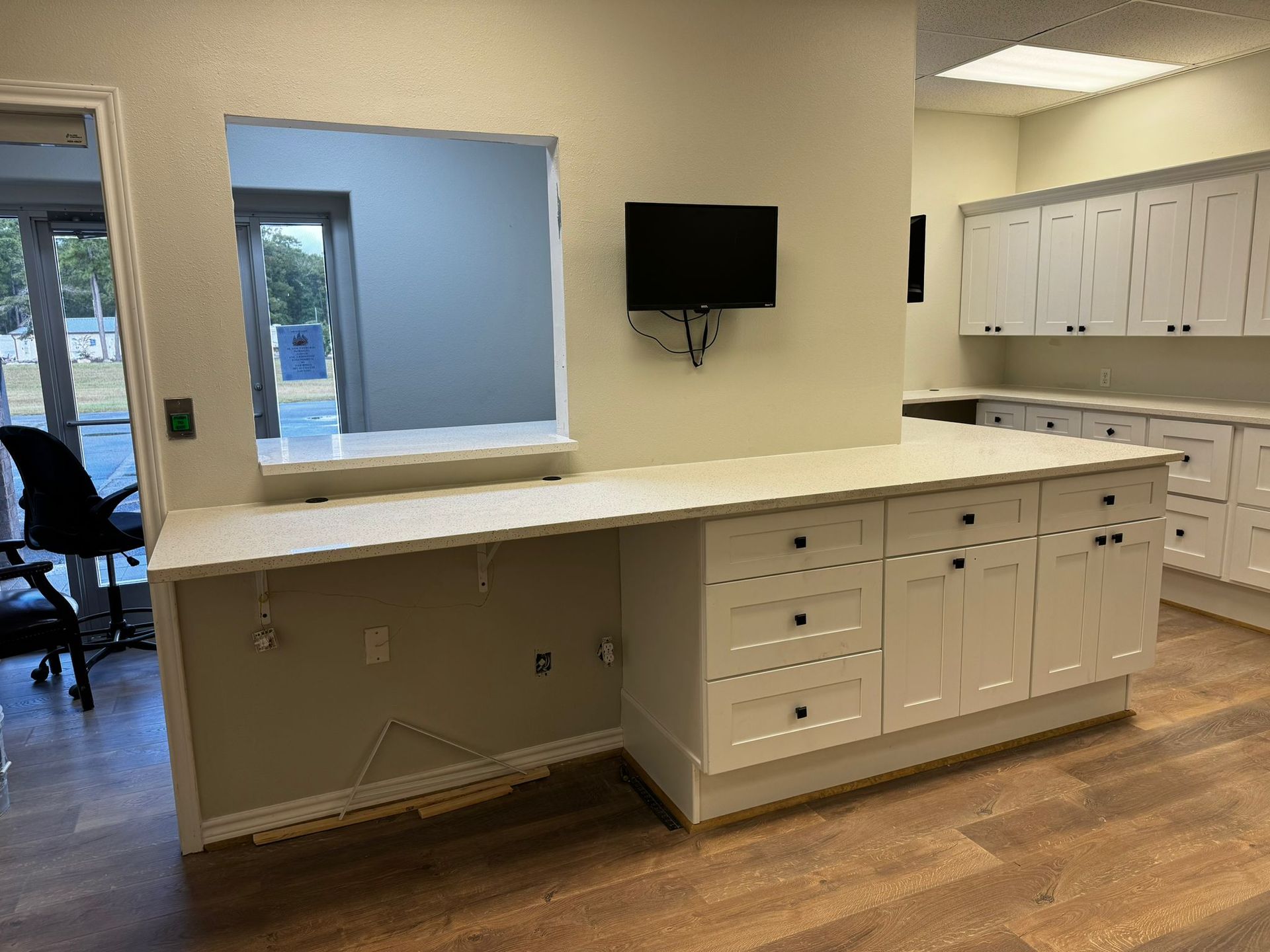 A kitchen with white cabinets and a flat screen tv on the wall.