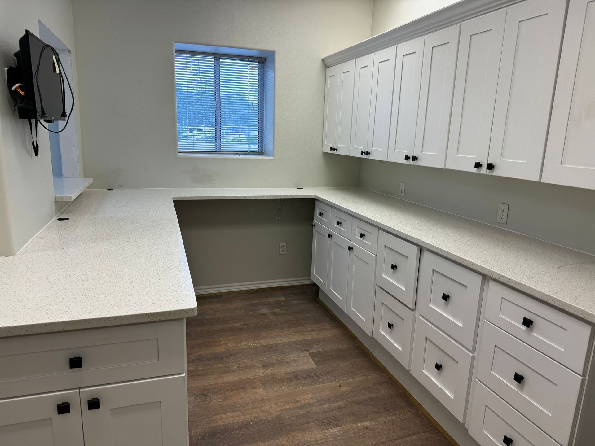 A kitchen with white cabinets , white counter tops , and a window.
