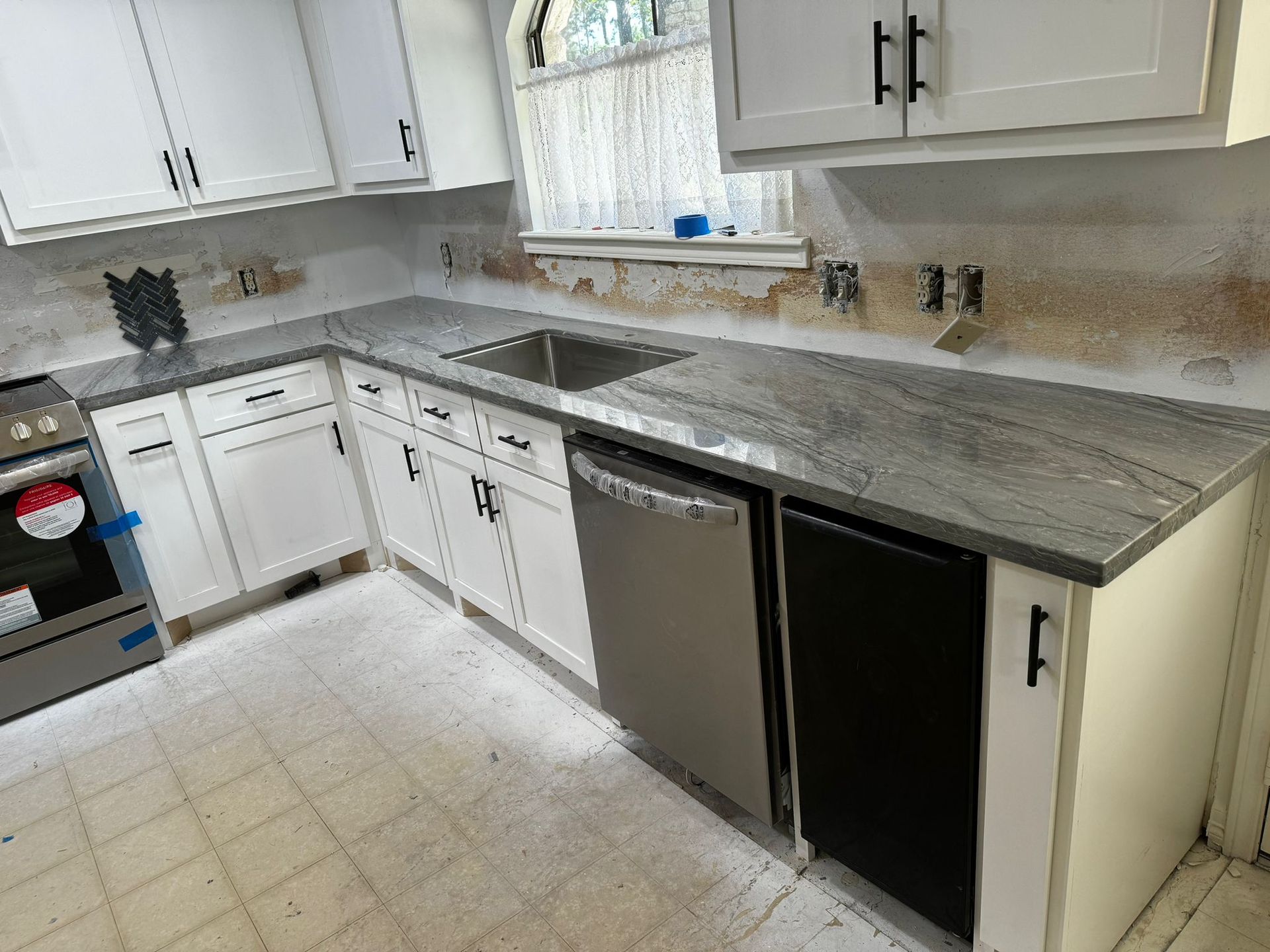 A kitchen with white cabinets , granite counter tops , stainless steel appliances and a black dishwasher.