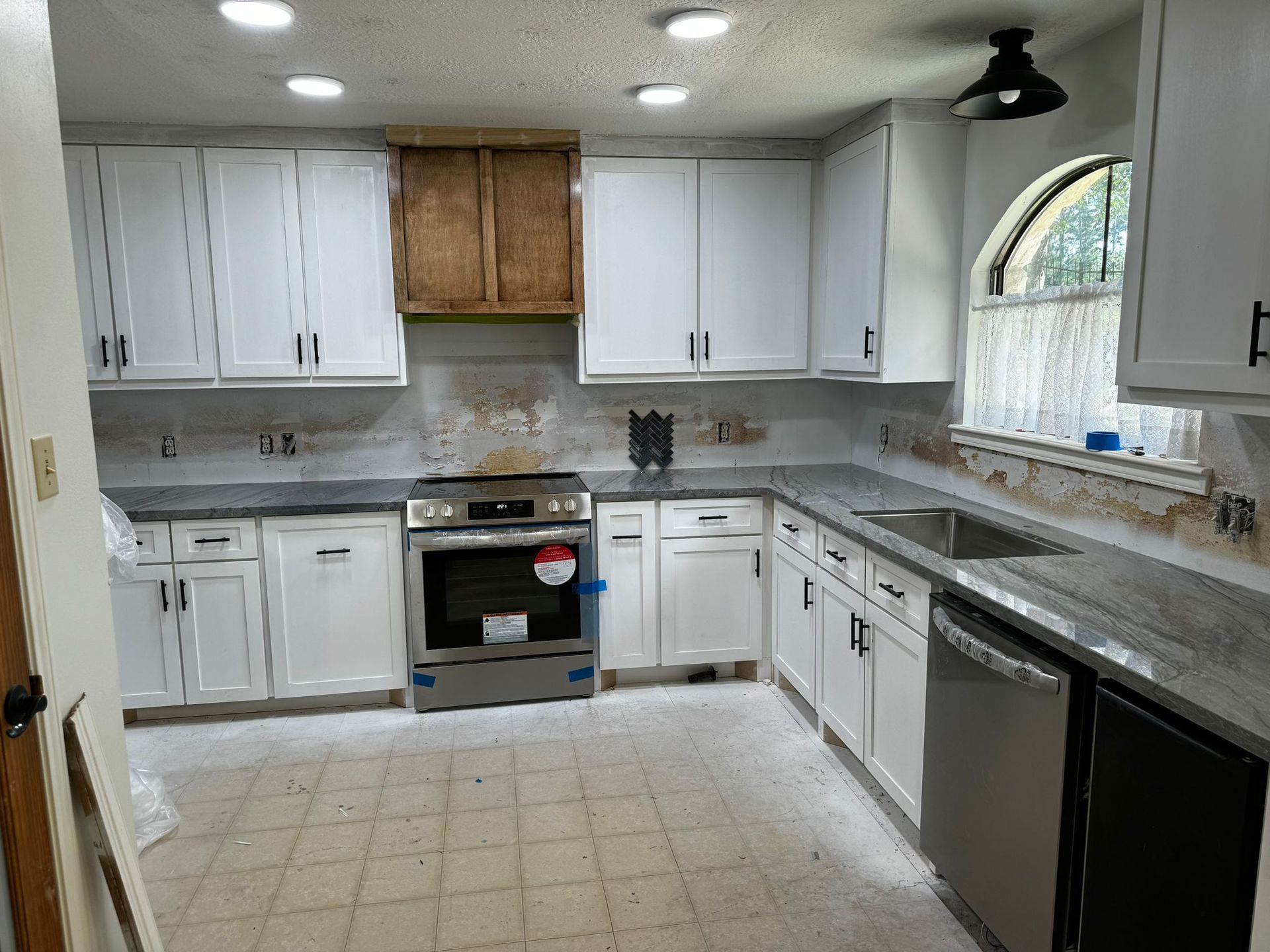 A kitchen with white cabinets , a stove , a sink , and a window.